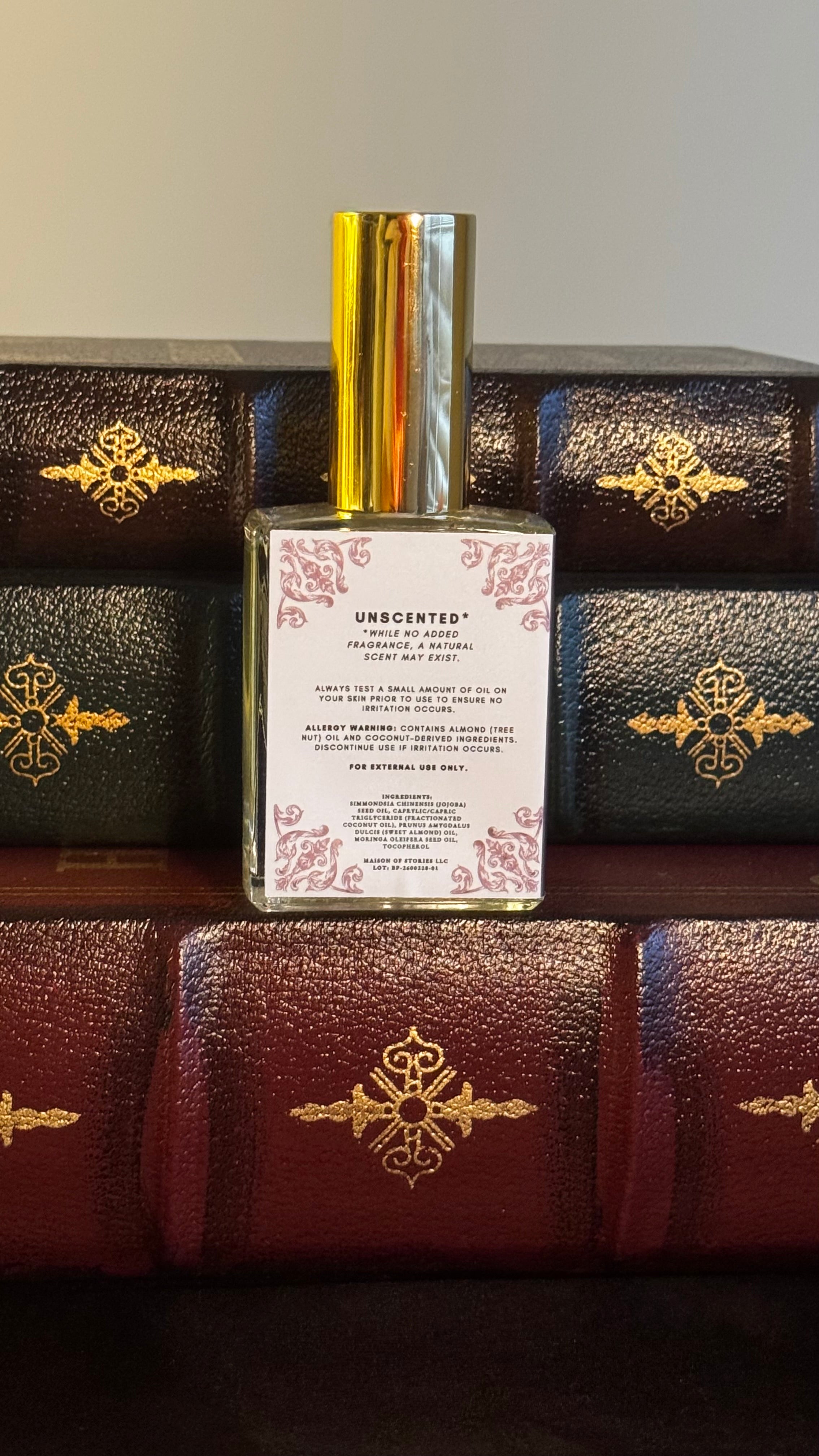 Back label of Maison of Stories Blank Page body oil 50ml with rococo floral corner details and unscented formula information, displayed on vintage leather-bound books