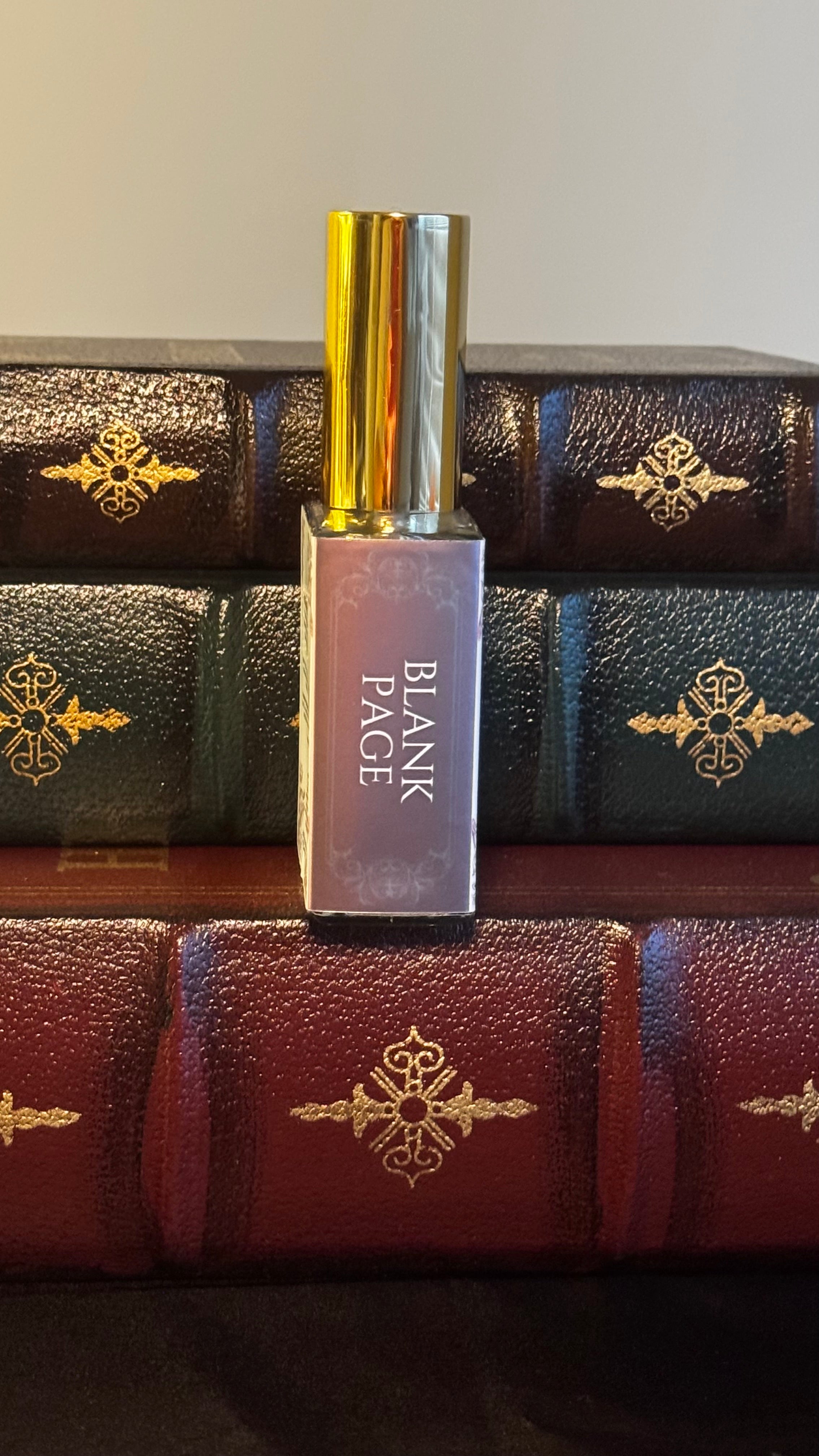 Maison of Stories Blank Page body oil 50ml spine view with mauve label showing scent name, displayed on vintage leather-bound books