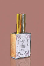 Clear glass bottle of Maison of Stories Blank Page body oil with gold cap against a dusty rose pink background