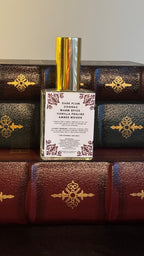 Back label of Maison of Stories Enemies to Lovers body oil 50ml with rococo floral corner details and dark plum, cognac, warm spice, vanilla praline and amber woods scent notes, displayed on vintage leather-bound books

