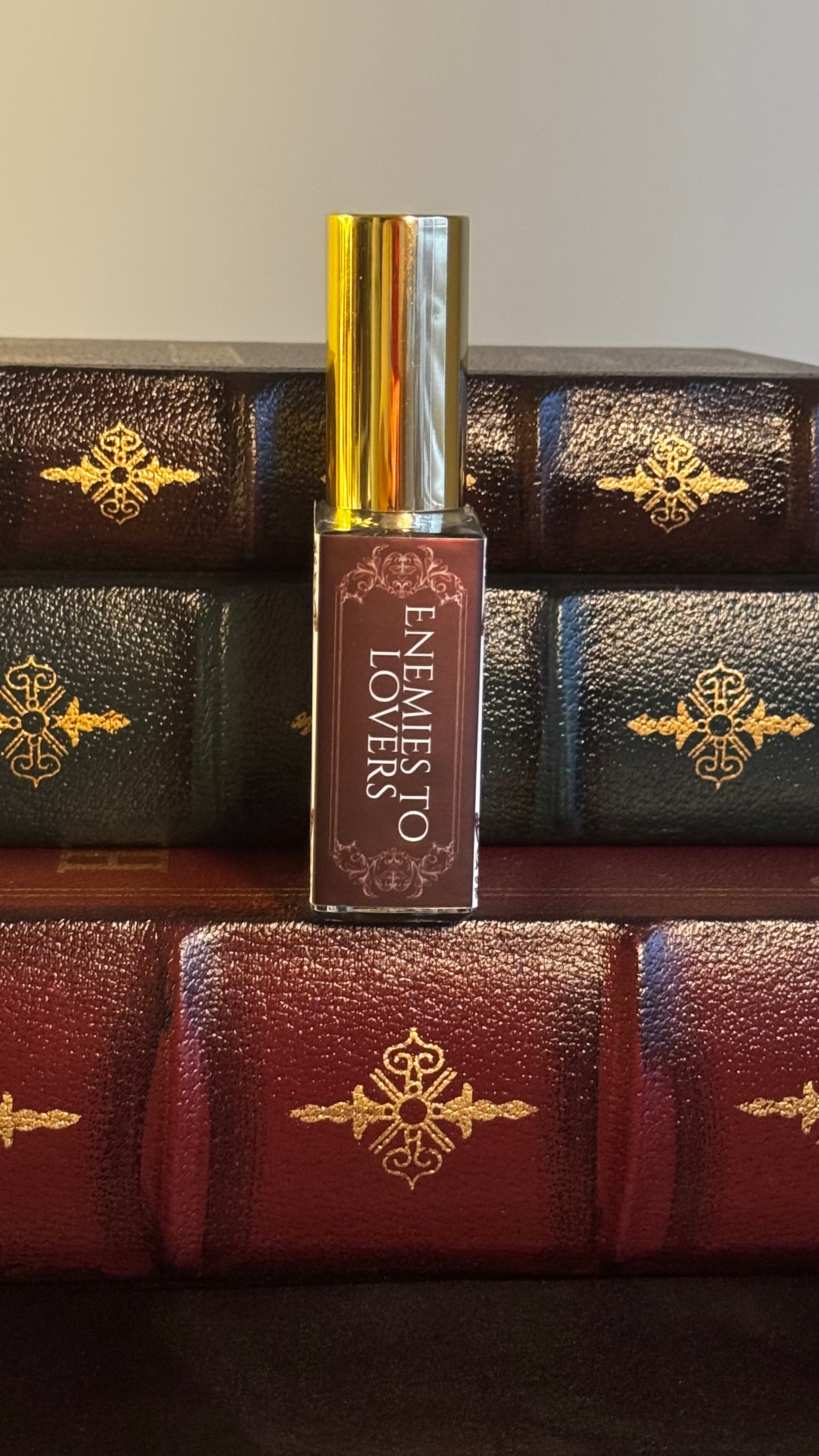 Maison of Stories Enemies to Lovers body oil 50ml spine view with oxblood label showing scent name, displayed on vintage leather-bound books