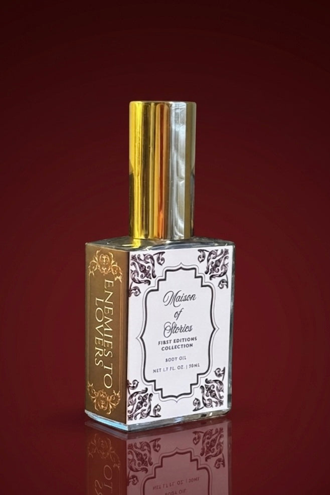 Maison of Stories Enemies to Lovers body oil glass bottle with gold spray cap set against a deep crimson background