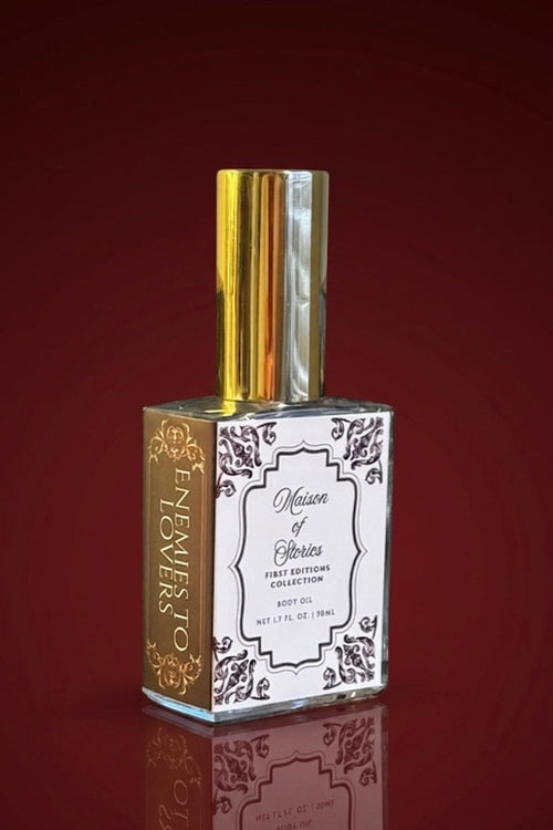 Maison of Stories Enemies to Lovers body oil glass bottle with gold spray cap set against a deep crimson background