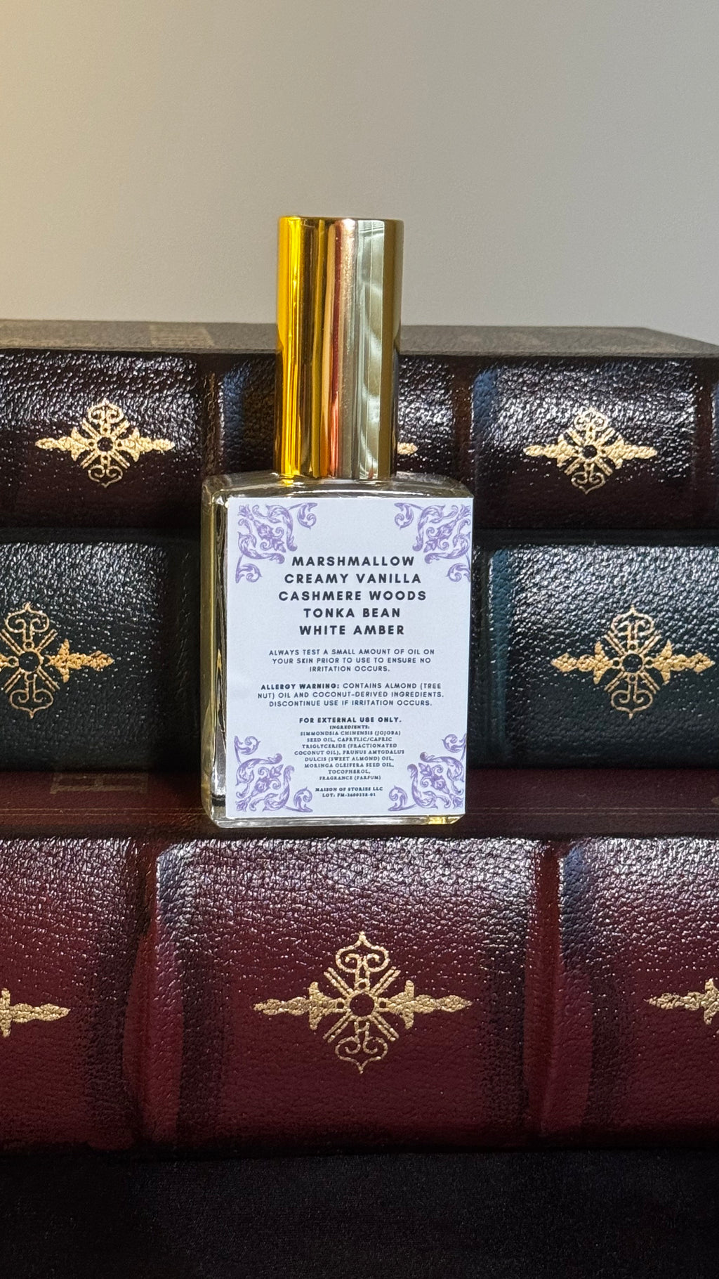 Back label of Maison of Stories Fated Mates body oil 50ml with rococo floral corner details and marshmallow, creamy vanilla, cashmere woods, tonka bean and white amber scent notes, displayed on vintage leather-bound books