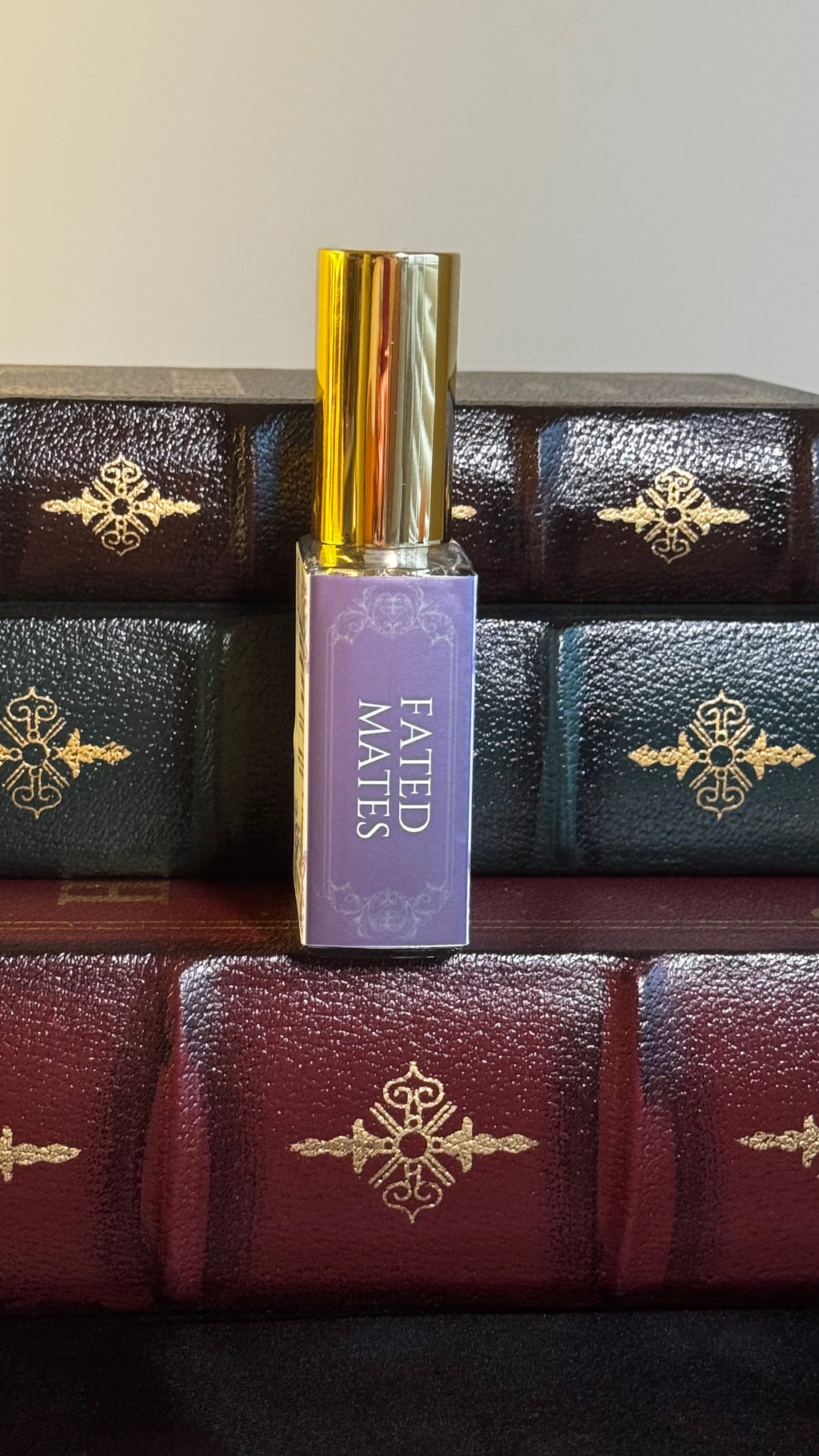 Maison of Stories Fated Mates body oil 50ml spine view with lavender label showing scent name, displayed on vintage leather-bound books