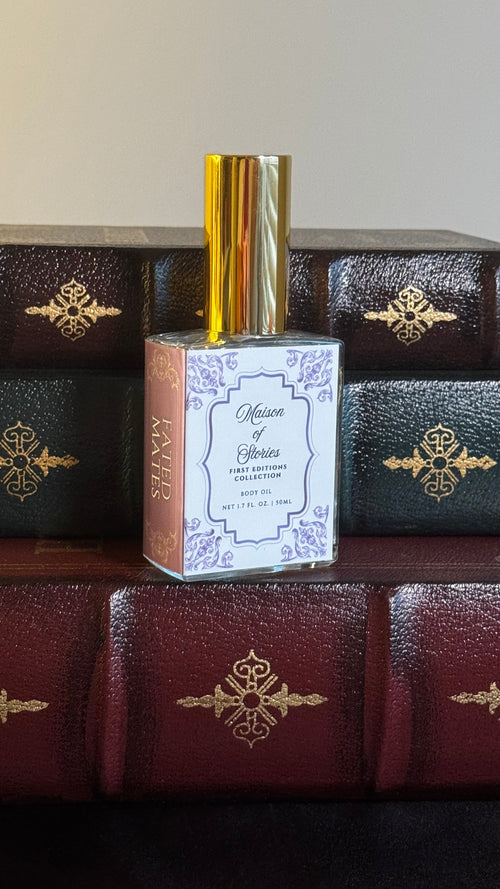 Maison of Stories Fated Mates body oil 50ml bottle with rococo floral label and gold cap, displayed on a stack of vintage leather-bound books