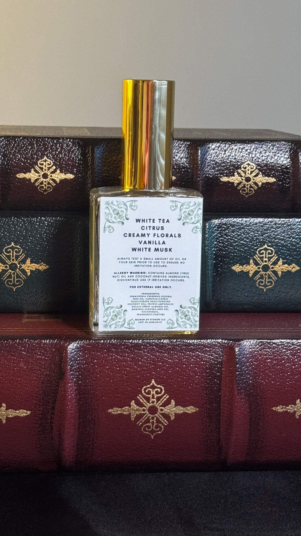 Back label of Maison of Stories Friends to Lovers body oil 50ml with rococo floral corner details and white tea, citrus, creamy florals, vanilla and white musk scent notes, displayed on vintage leather-bound books