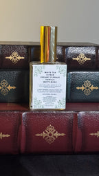 Back label of Maison of Stories Friends to Lovers body oil 50ml with rococo floral corner details and white tea, citrus, creamy florals, vanilla and white musk scent notes, displayed on vintage leather-bound books