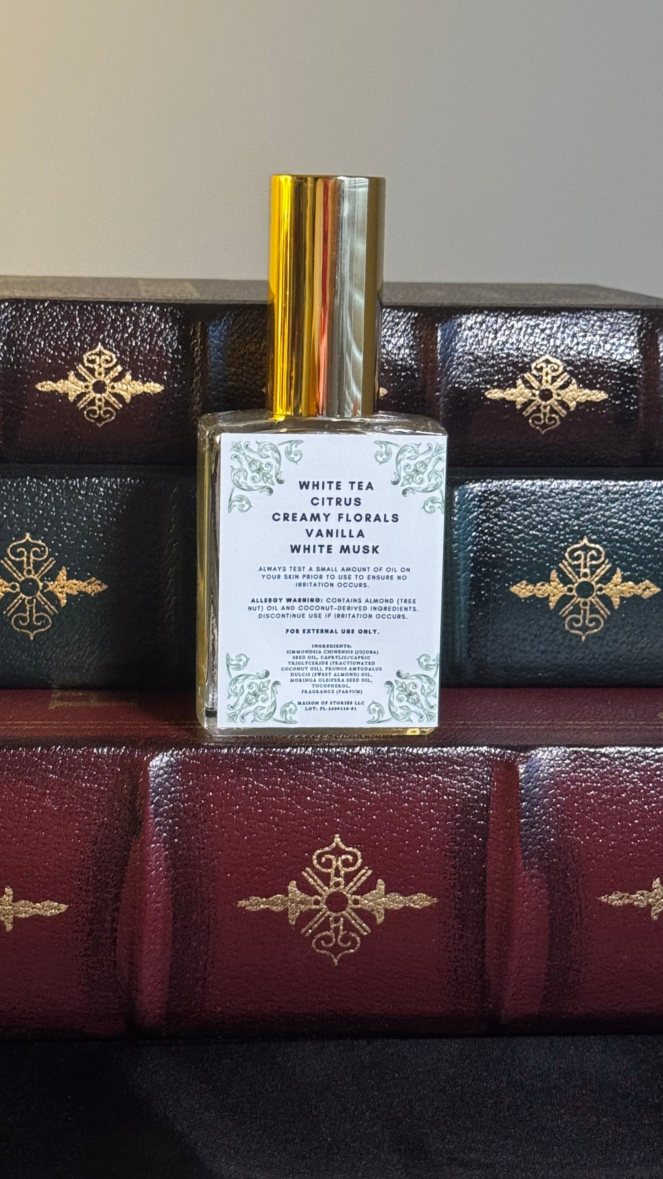 Back label of Maison of Stories Friends to Lovers body oil 50ml with rococo floral corner details and white tea, citrus, creamy florals, vanilla and white musk scent notes, displayed on vintage leather-bound books