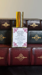 Back label of Maison of Stories Love Triangle body oil 50ml with rococo floral corner details and pink pepper, white florals, sandalwood, patchouli and warm amber scent notes, displayed on vintage leather-bound books