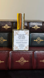Back label of Maison of Stories Slow Burn body oil 50ml with rococo floral corner details and Tahitian vanilla, sugarcane, warm amber, velvet woods and white musk scent notes, displayed on vintage leather-bound books