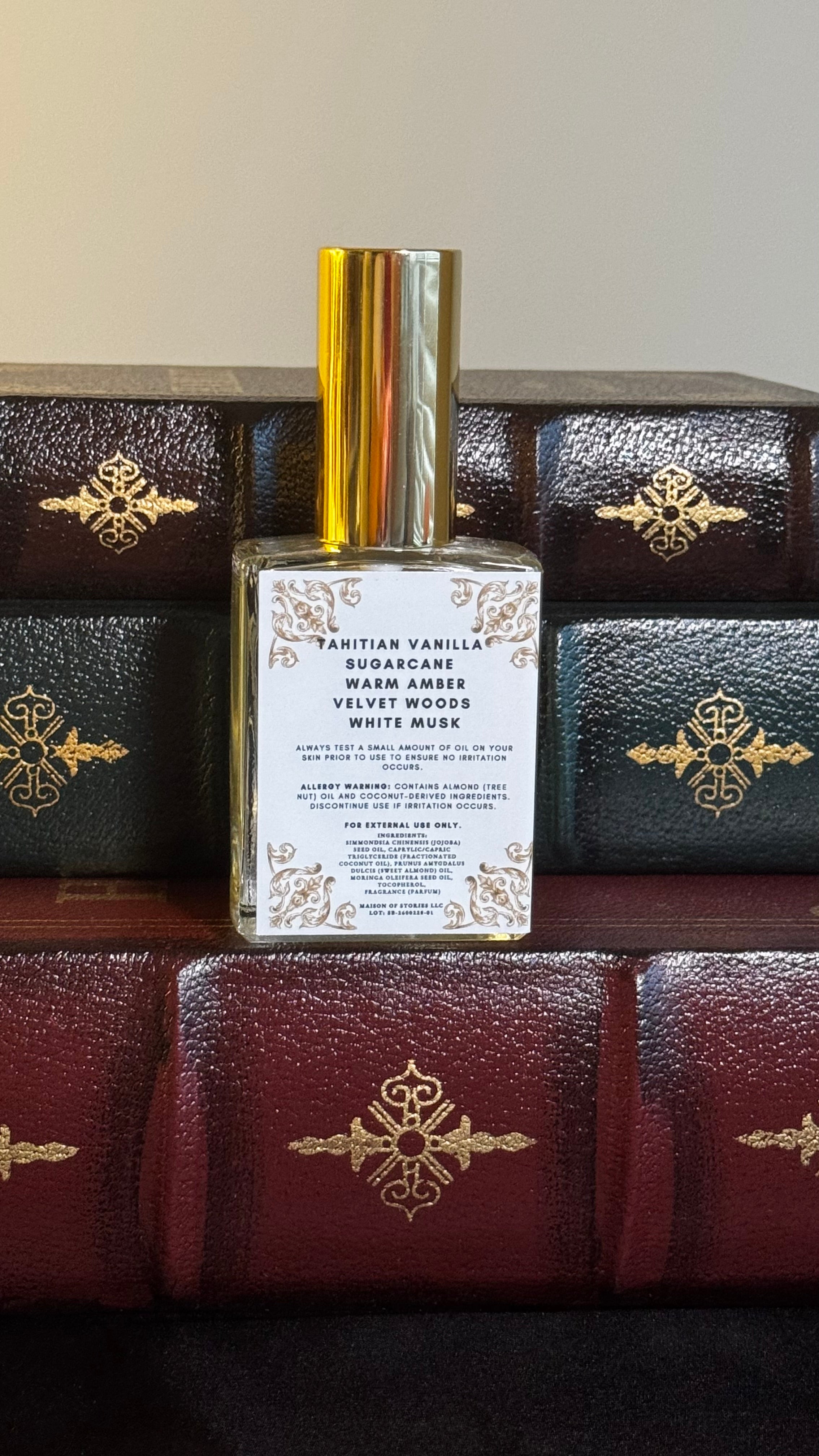 Back label of Maison of Stories Slow Burn body oil 50ml with rococo floral corner details and Tahitian vanilla, sugarcane, warm amber, velvet woods and white musk scent notes, displayed on vintage leather-bound books